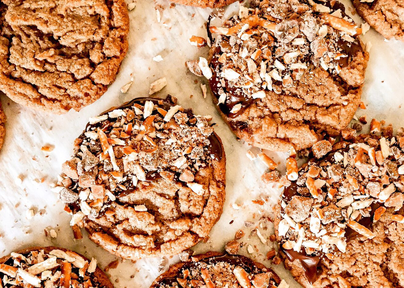 a tray of freshly baked peanut butter cookies dipped in chocolate and topped with crushed toffee and pretzels.