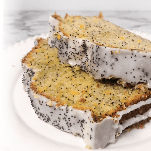 A white plate with 2 slices of lemon poppyseed cake with a crunchy sugary glazed sprinkled with more poppyseeds.