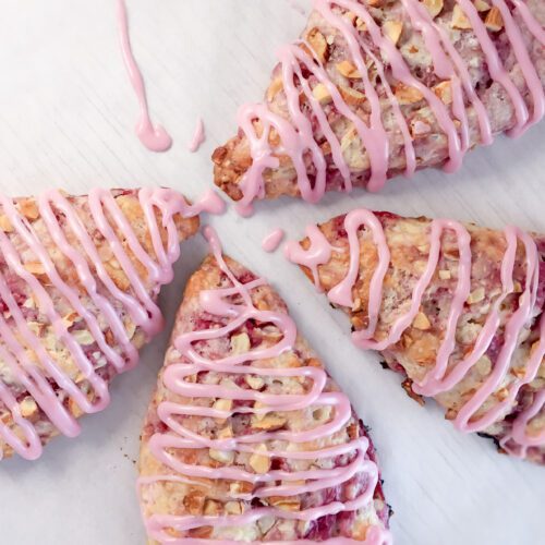 a tray with 4 freshly baked raspberry scones drizzled with a raspberry glaze.