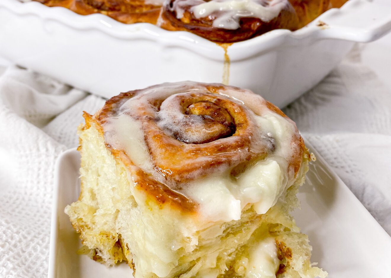 cinnamon roll on a plate slathered with cream cheese frosting.